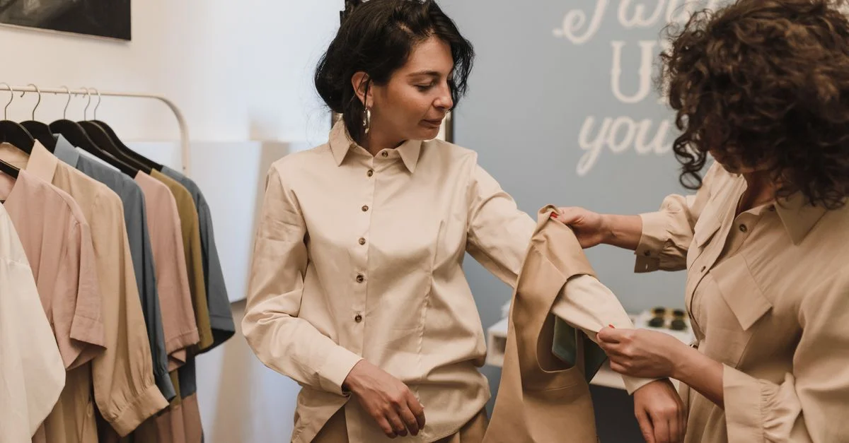 Dos mujeres comprando en una boutique, examinando una camisa juntas entre una selección de ropa elegante.