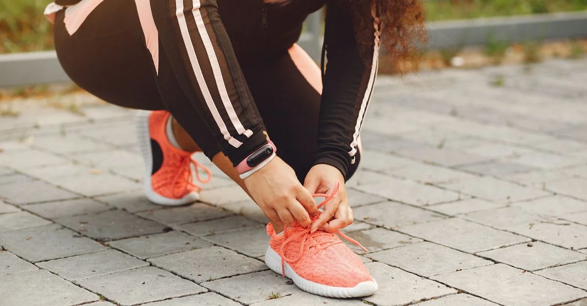 Una mujer atándose los cordones en una acera de ladrillos, lista para hacer ejercicio al aire libre.