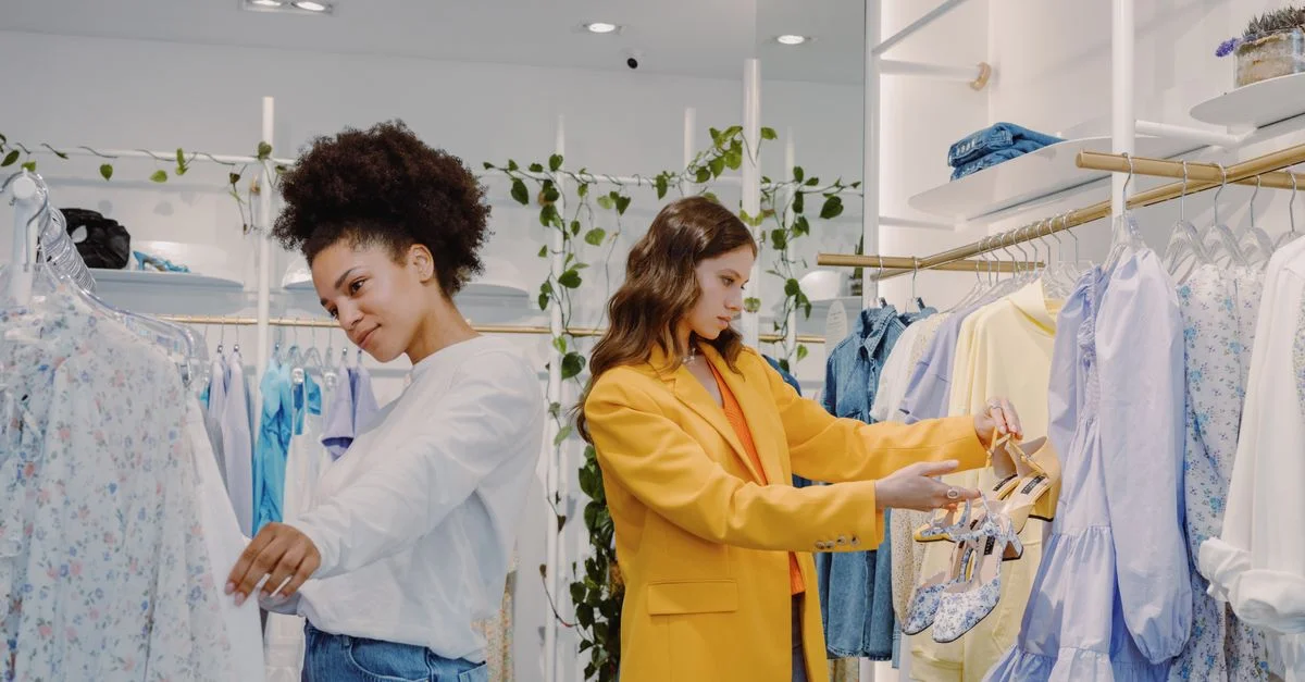 Dos mujeres comprando en una tienda de ropa moderna, mirando atuendos elegantes.