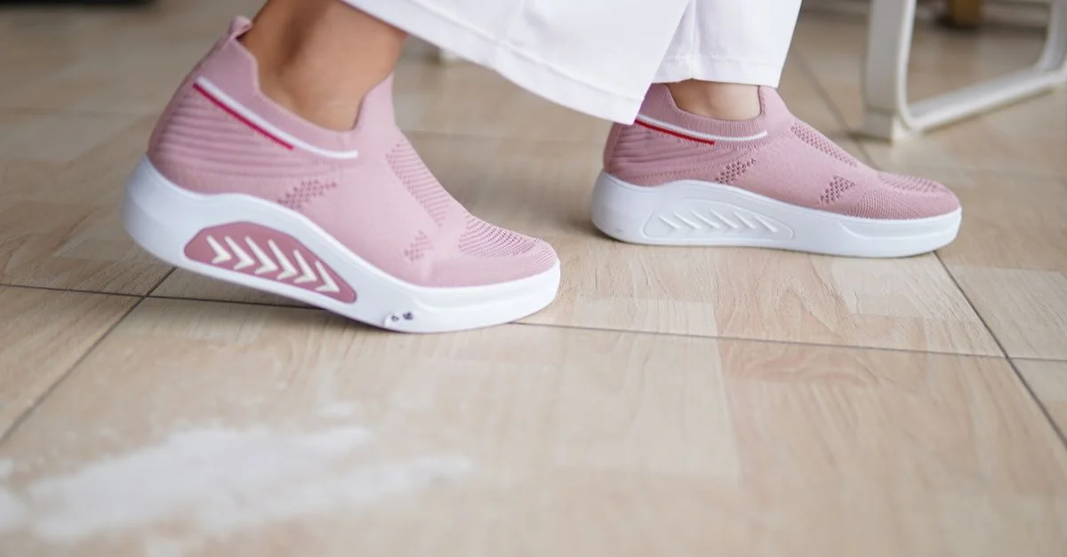 Primer plano de zapatillas rosa a la moda usadas en interiores sobre un suelo de madera.