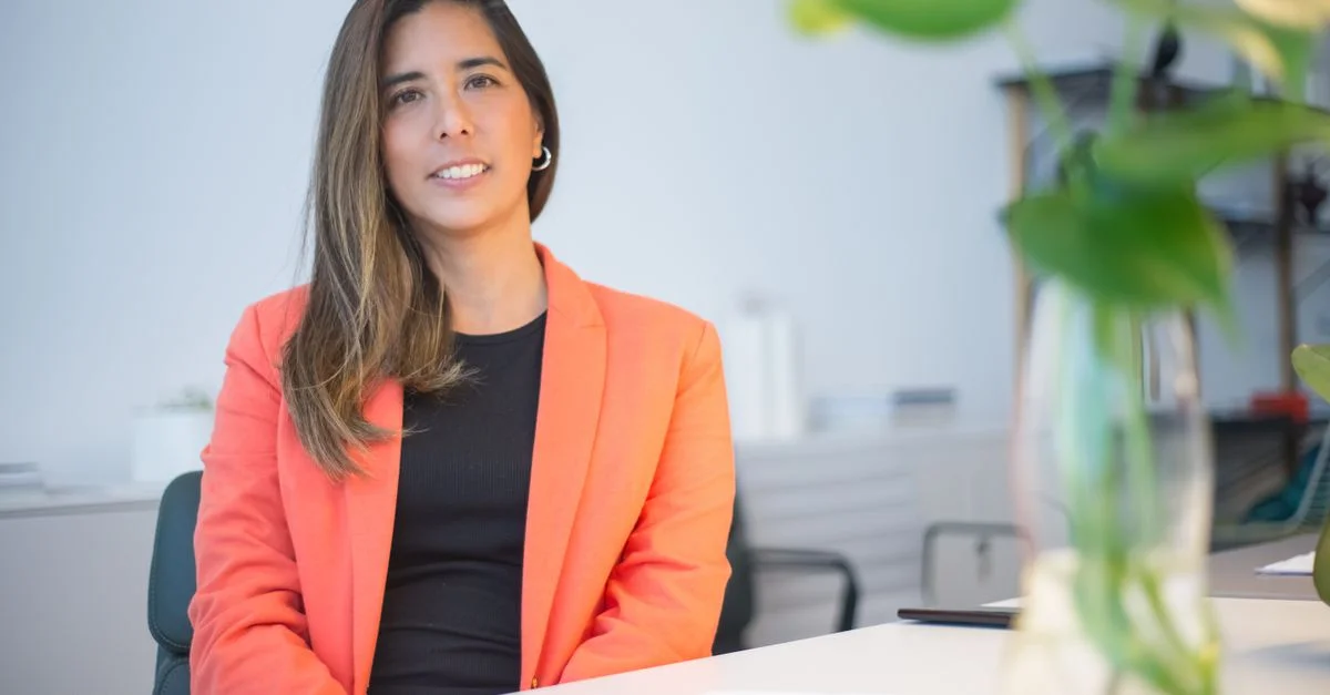Mujer de negocios segura vestida con un blazer, sentada en un escritorio en un entorno de oficina.