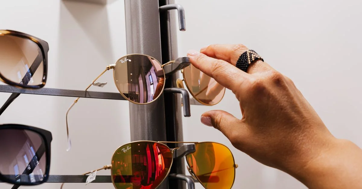 Close-up de una mano seleccionando gafas de sol de una exhibición de venta al por menor con múltiples opciones disponibles.