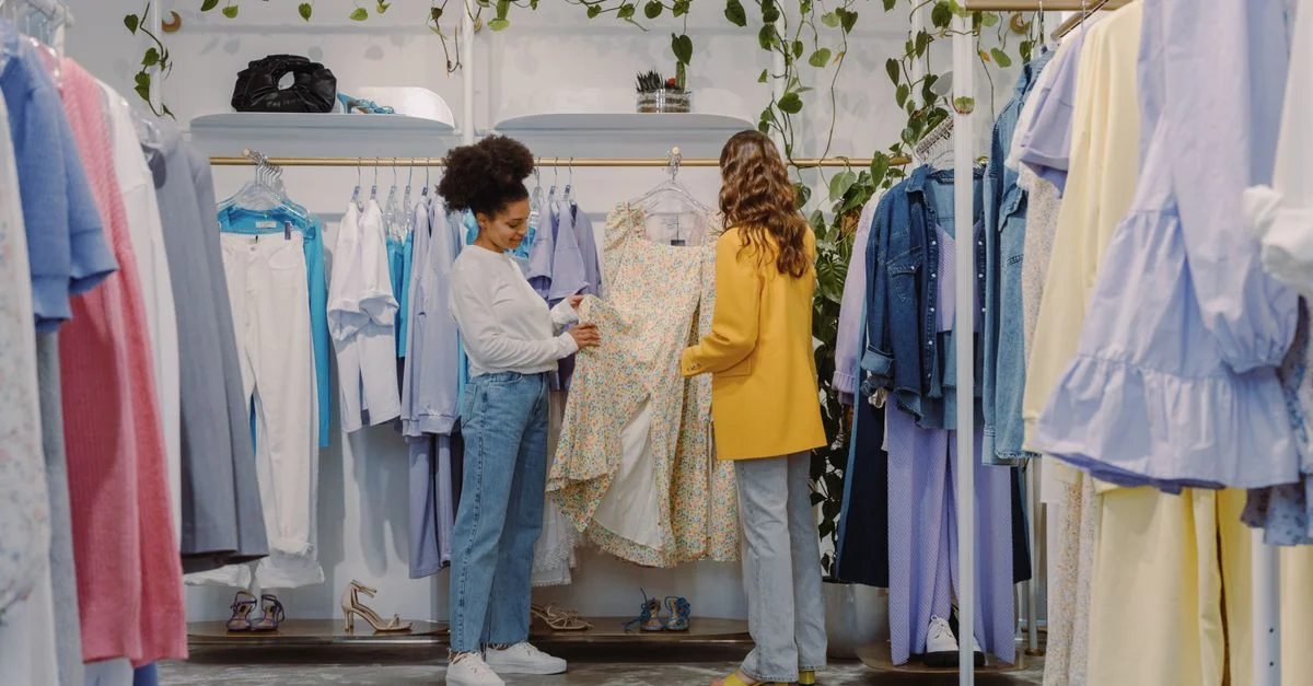 Dos mujeres comprando conjuntos modernos en una boutique de ropa contemporánea llena de prendas coloridas.