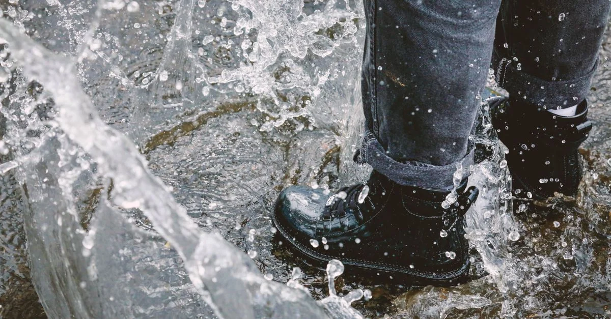 Un primer plano de una persona pisando en el agua con botas impermeables, capturando un salpicón juguetón.