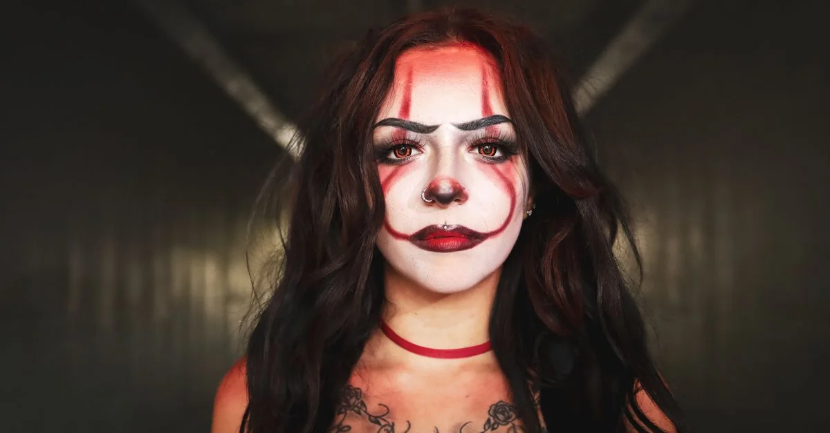 Un retrato dramático de una mujer con maquillaje de payaso y pecho tatuado, capturado en interiores.