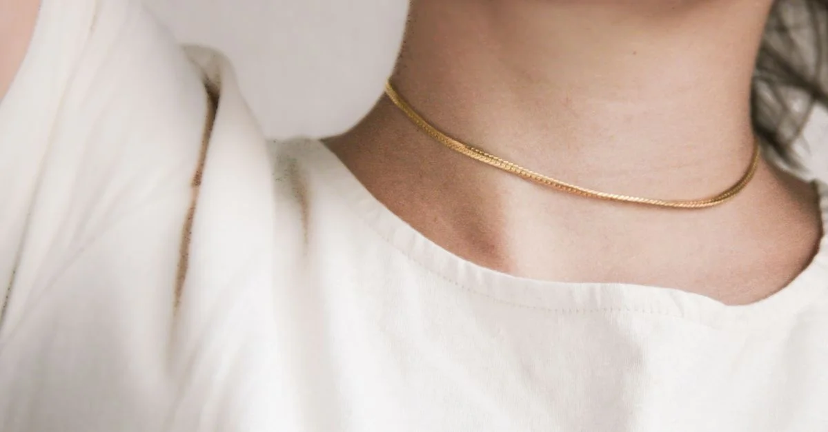 Primer plano minimalista de un collar de oro en el cuello de una persona que lleva una camisa blanca.